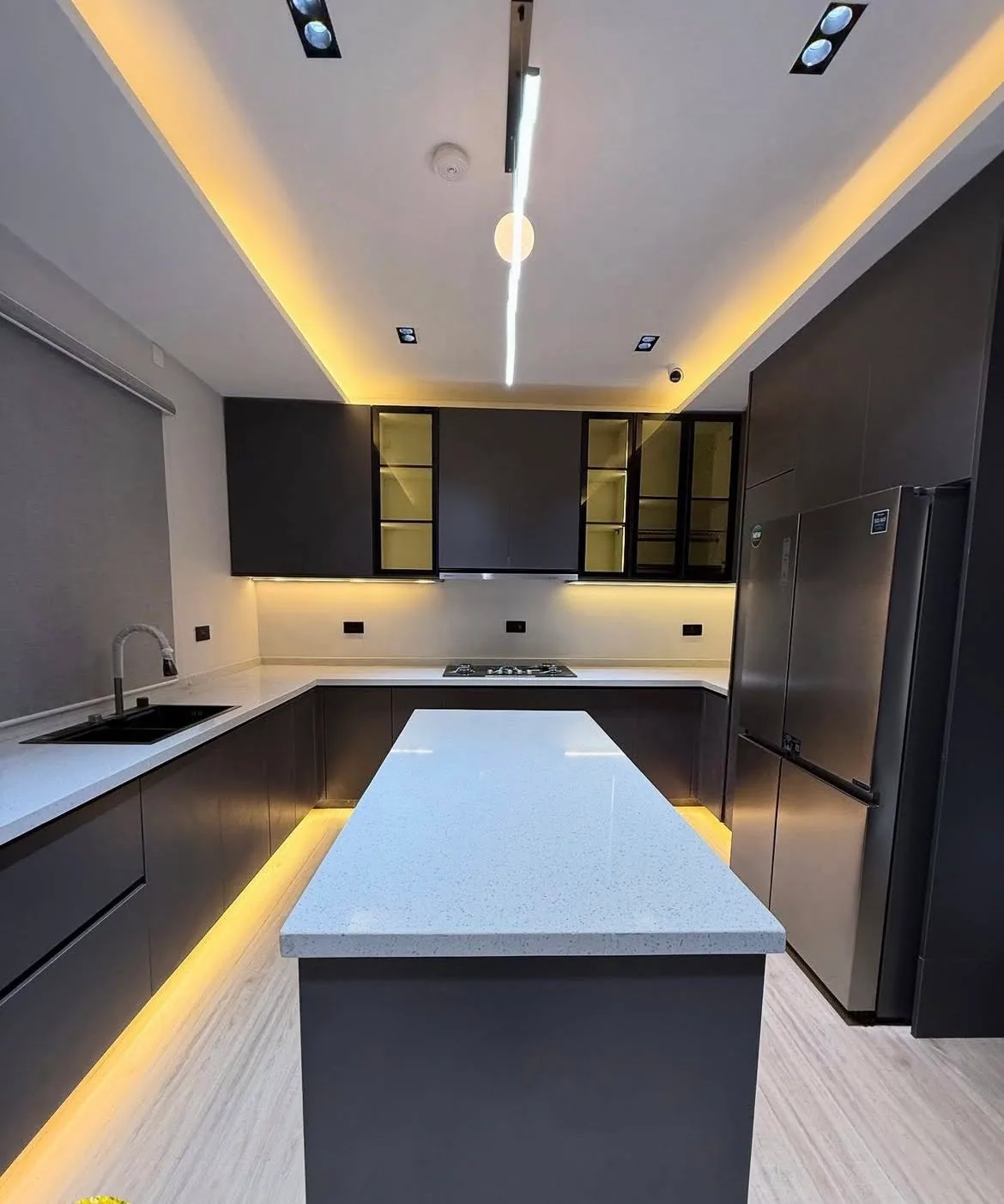 Dark grey U-shaped kitchen with white quartz countertops, LED under-cabinet lighting, glass-front upper cabinets, and center island